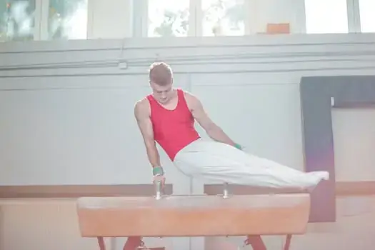 A male gymnast demonstrates strength and agility practicing on a pommel horse indoors.